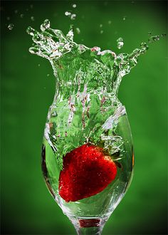 ripe strawberry dunked in a glass of water against a green background